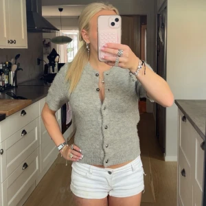 Grå kortärmad kofta med knappar - Supermysig grå kofta från Gina tricot med korta ärmar och rund hals. Koftan är stickad i mjukt material och har snygga silvriga knappar framtill. Perfekt att styla med jeans eller shorts för en chill look.