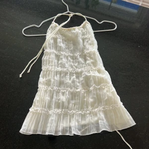 Vit halterneck blus från Gina Tricot - Supersöt vit blus från Gina Tricot i storlek L. Blusen har omlott-design med snörning i nacken och ryggen, plisserade volanger och ett skirt, glansigt material i polyester. Perfekt för festtillfällen när du vill känna dig extra fin.😇// den passar även bra på s/m 