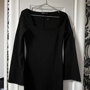 Svart långärmad klänning fyrkantig urringning Boohoo - Snygg svart klänning från Boohoo med lång ärm och fyrkantig urringning. Modellen är figurnära och har en stilren, minimalistisk look som passar perfekt när du vill känna dig extra chic. Materialet är mjukt och stretchigt för en bekväm passform.