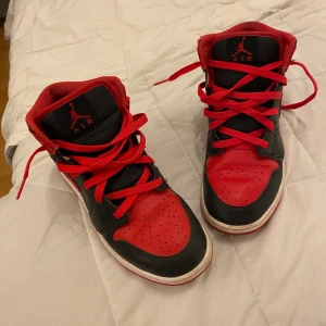 Nike Air Jordan 1 Bred Highs - Säljer ett par ikoniska Nike Air Jordan 1 Highs i svart och rött skinn. Klassisk Bred-färgway med röda snören, svart Swoosh och röd yttersula. Perfekta för dig som vill sticka ut med en tidlös sneakerlegend.