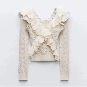 Stickad tröja med volang från ZARA - Supersöt beige stickad tröja från ZARA med v-ringning och spetsvolanger framtill. Tröjan har lång ärm och ett fint mönster. Väldigt sparsamt använd och har inga defekter! 