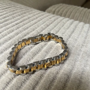  länkarmband i guld och silver - Snyggt länkarmband från  i klassisk design med guldfärgade och silverfärgade länkar. Armbandet har den ikoniska -kronan i guld på två ställen och en smidig låsanordning. Perfekt för dig som gillar exklusiva detaljer och stilren look.