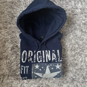 Marinblå hoodie med stjärntryck - Snygg marinblå hoodie från ORIGINAL med stort tryck framtill: 'ORIGINAL FIT EST. 2024'. Inte använd mycket, har inga hål eller fett fläckar! Ordinarie pris: 935kr 