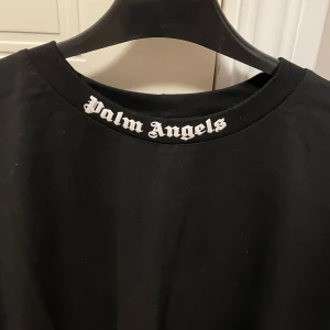 Svart Palm Angels t-shirt med tryck - Svart t-shirt från Palm Angels med stort vitt logotryck på framsidan och mindre tryck i nacken. Oversized passform och klassisk rund hals. Tillverkad i mjuk bomull, perfekt för en streetwear-look.