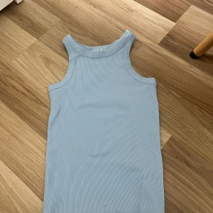 Ljusblå ribbad linnetopp KapAhl - Supersöt ljusblå ribbad linnetopp från KappAhl. Modellen är ärmlös med breda axelband och rundad halsringning. Perfekt för varma dagar och enkel att matcha med jeans eller shorts.