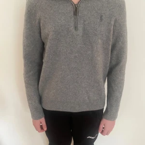 Grå halvziptröja från Ralph Lauren - Snygg grå stickad tröja från Ralph Lauren med half zip-dragkedja och diskret logga på bröstet. Tröjan har lång ärm och är i mjukt ullmaterial, perfekt för kyliga dagar. Enkel och stilren design som funkar till det mesta. Storlek L men har krympt till xxs/xs.
