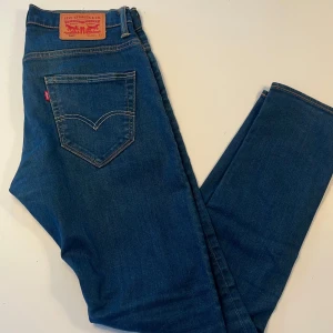 Levi's 520 blå jeans W29 L32 - Säljer ett par klassiska Levi's 520 jeans i snygg blå tvätt. Jeansen har normal passform, raka ben och klassiska bakfickor med kontrastsömmar. Perfekta för dig som gillar en tidlös denimlook. Märke på bakfickan och läderpatch i midjan.