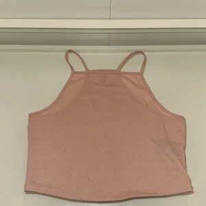 Rosa croppad linnetopp från H&M Divided - Säljer en ljusrosa croppad linnetopp från H&M Divided. Toppen har smala axelband och ärmlös design med rak nederkant. Tillverkad i mjuk bomullsmix som känns skön mot huden. Perfekt för varma dagar eller att styla lager på lager.