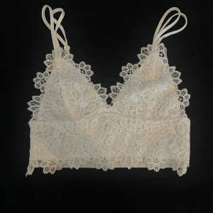 Vit spetsig linnetopp från Bik Bok - Superfin vit linnetopp från Bik Bok med tunna axelband och detaljerad spets framtill. Toppen har en mjuk satinliknande baksida och spetskant runt hela överdelen. Perfekt för lager-på-lager eller som statement piece till jeans eller kjol.