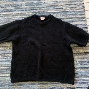 Svart stickad tröja Gina Tricot - En svart stickad tröja från Gina Tricot med rund halsringning och kortare ärmar. Enkel och stilren modell som är lätt att matcha med olika outfits. Perfekt för dig som gillar en clean och klassisk look.