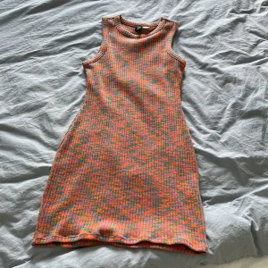 Färgglad ribbad klänning från H&M Divided - Säljer en ribbad kortklänning från H&M Divided i storlek XS. Klänningen har ett coolt mönster i orange, rosa och grönt, är ärmlös och har rund hals. Perfekt för dig som gillar färg och vill sticka ut lite extra.