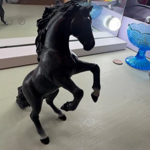 En av mina schleich hästar som jag haft ett tag nu och som jag börjar tröttna på❤️🙈 ordinarie pris är 89kr och jag säljer den nu för 20 kronor som jag tycker är ett ganska bra pris, skriv om ni vill att jag sänker priset - Bilderna visar en svart hästfigur i plast eller liknande material, stående på bakbenen. Det finns ingen bok synlig på bilderna, endast en häststatyett och några dekorativa föremål i bakgrunden.