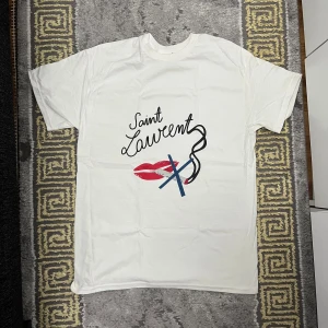 Saint Laurent ”No Smoking” T shirt - Vit t-shirt från Saint Laurent med coolt grafiskt tryck framtill. Trycket består av svarta bokstäver, röda läppar och blå detaljer. T-shirten har rund hals och korta ärmar, tillverkad i mjuk bomull. Perfekt för dig som gillar statement-plagg. Storlek M, aldrig använd