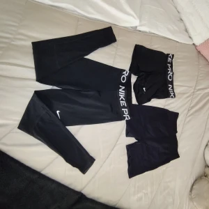 Nike Pro svarta tights & shorts - Säljer ett set med svarta Nike Pro tights och två par svarta shorts. Tightsen har Nike Pro-logga och en tight passform, perfekta för träning. Ett par shorts har också Nike Pro-logga i midjan, det andra paret är enkla svarta cykelshorts. Snygga och sportiga! PRIS KAN DISKUTERAS!!!! (Använt max 5 ggr)