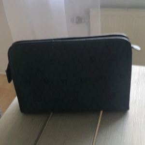 Svart  nesesär dior med mönster - Snygg svart nesäsär från Dior med hexagonmönster och små loggor över hela ytan. Plånboken har dragkedja runtom och är tillverkad i slitstark polyester. Perfekt för att hålla koll på kort och cash med stil.