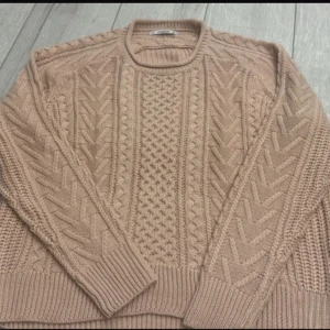 Beige stickad tröja med mönster - Säljer en beige stickad tröja med snyggt strukturmönster och rund hals. Tröjan har långa ärmar och breda ribbade muddar vid ärmslut och nederkant. Perfekt för dig som gillar mysiga och stilrena plagg med lite extra detaljer.