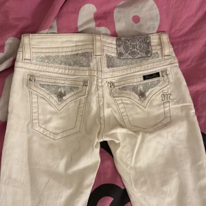 Vita Miss Me jeans med glitterdetaljer - Snygga vita jeans från Miss Me med glittriga detaljer på fickorna och bakstycket. Byxorna är orginailt skinny men sydd till bootcut. dekorativa sömmar och coola knappar med bling. Perfekta för dig som vill sticka ut med en unik och trendig look.