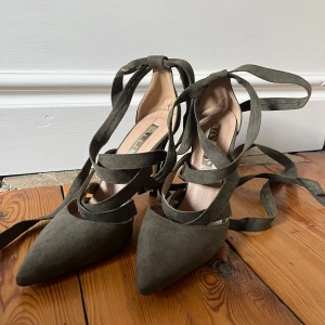 Olivgröna klackskor - Snygga olivgröna klackar från Billini i mocka med spetsig tå och hög klack. Skorna har långa remmar som snörs runt vristen. Klacken är 10 cm. 