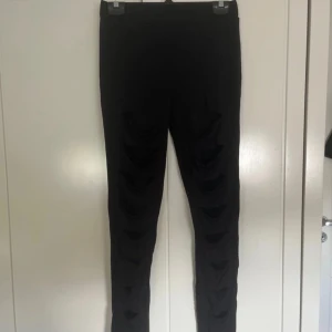 Svarta leggings med mesh och slitsar - Svarta leggings från Forplay med coola slitsar framtill och meshdetaljer under. Tight passform och stretchigt material som sitter snyggt. Perfekta för dig som vill ha en edgy vibe och sticka ut lite extra.