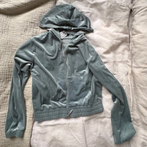 Ljusblå velour hoodiejacka M - Supermjuk ljusgrå hoodiejacka i velour med dragkedja framtill och kängurufickor. Jackan har ribbade muddar och en avslappnad passform, perfekt för en chill look. Snygg och enkel att matcha med dina favoritjeans eller mjukisbyxor. Den är aldrig använd och har lappen kvar! Färgen skulle jag beskriva som turkos ungifär kanske något mer åt de blåare hållet.💕💕💕