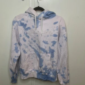 Blåvit tie-dye hoodie Sweet Sktbs - Snygg hoodie från Sweet Sktbs i blå och vit tie-dye. Tröjan har broderad logga på bröstet, stor huva med snörning och en klassisk känguruficka. Mjuk bomullskänsla och ribbade muddar vid ärmslut och nederkant. Perfekt för chill dagar.