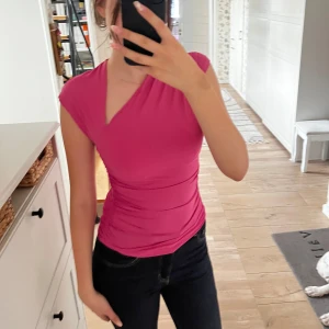 Rosa omlottopp från Zara - Rosa omlottopp från Zara med asymmetrisk v-ringning och tight passform. Toppen har korta ärmar och är gjord i mjukt polyester-material som sitter skönt mot kroppen. Den är dessutom väldigt skön mot huden och man har inga problem med att vara rörlig i den.
