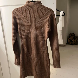 Brun ribbad stickad klänning - Säljer en brun stickad klänning med ribbad struktur och lång ärm. Klänningen har en hög krage och är figurnära med snygga detaljer i stickningen. Använd enstaka gång 