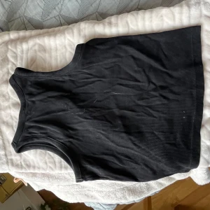 Svart ribbad linnetopp - En svart ribbad linnetopp med rund halsringning och ärmlös design. Perfekt att matcha med jeans eller kjol för en enkel och stilren look. Mjuk och stretchig känsla som sitter snyggt på kroppen.