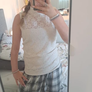 Vit spetsblus från Gina Tricot - Supersöt vit blus från Gina Tricot i spets med hög hals och ärmlös design. Blusen har ett romantiskt blommönster i spetsen och sitter snyggt figurnära. Perfekt att styla med jeans eller kjol för en fräsch look.