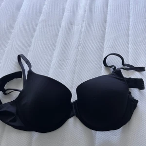 Svart BH från Lilja - En klassisk svart BH från Lilja. Den har släta kupor, justerbara axelband och hakknäppning bak. Perfekt under tighta toppar för en clean look. Materialet är mjukt och följsamt för extra komfort. Vid frågor hör av dig!