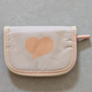 Liten beige necessär med hjärtan  - HELT OANVÄND NECESSÄR. Söt liten beige necessär med persikofärgade hjärtan på utsidan och praktisk dragkedja. Insidan har meshficka och fack för förvaring. Perfekt storlek för att ha med sig överallt.