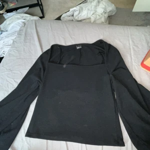 Svart långärmad topp Gina Tricot - En svart långärmad topp från Gina Tricot med fyrkantig urringning. Enkel och stilren design som passar till många olika looks. Mjuk och stretchig känsla, perfekt att matcha med jeans eller kjol.