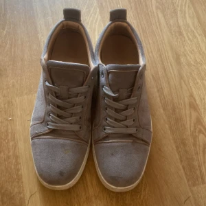 Louboutins - Snygga grå sneakers i mocka med klassisk snörning och vit sula. Skorna har en unik röd undersida som ger en cool kontrast. Perfekta för dig som gillar stilrena men ändå lite annorlunda skor.