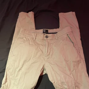 Beige chinos från Cubus, stl 28 - Snygga beige chinos från Cubus i ekologisk bomull med lite stretch. Klassisk rak passform med fickor på sidorna och bak, samt hällor för bälte. Perfekta för en clean och avslappnad look.