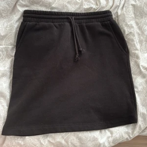 Svart kortkjol från Pieces med snörning - Svart kortkjol från Pieces i mjukt sweatshirtmaterial. Kjolen har resår i midjan med snörning och praktiska fickor på sidorna. 