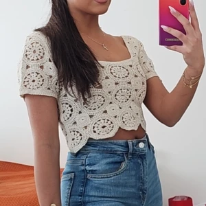 Beige virkad croppad blus - Superfin beige virkad blus med korta ärmar och croppad passform. Toppen har ett unikt cirkelmönster och söt vågig kant nertill. Perfekt för dig som gillar boho-stil och vill sticka ut med en cool och luftig topp i sommar.