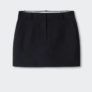 Svart kortkjol från MNG - Stilren svart kortkjol från MNG med klassisk rak passform och hällor för bälte. Kjolen har diskreta fickor bak. Perfekt för dig som gillar minimalistisk och clean stil. Aldrig använd, nypris 600kr