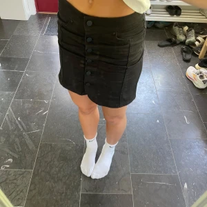 Svart jeanskjol med knappar, strl 34 - Snygg svart jeanskjol från g perfect jeans i storlek 34. Kjolen är kort och har en rak passform med knappar framtill och klassiska jeansfickor. Passar perfekt till sneakers eller boots.