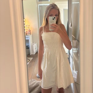 Vit kort klänning från H&M Divided - Supersöt vit klänning från H&M som jag aldrig har andvänt, Divided med smock upptill och tunna axelband. Klänningen har diskreta prickar i tyget och knytband på ryggen. Perfekt för varma dagar och har en luftig, flowy passform som känns riktigt fräsch.