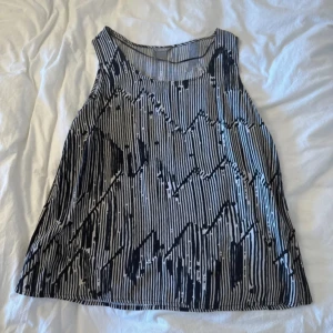 Randig ärmlös linnetopp från Lindex - Säljer en luftig och snygg ärmlös linnetopp från Lindex med svartvitt randigt mönster och grafiska detaljer. Toppen har rund halsringning och är perfekt för dig som gillar en avslappnad men cool stil.