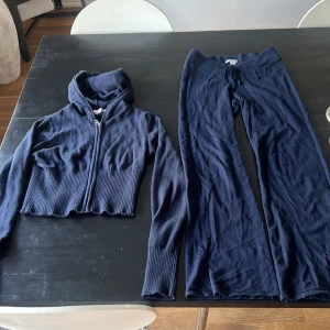 Mörkblå stickade mjukisbyxor och tröja från Gina Tricot - Mörkblå stickade mjukisbyxor från Gina Tricot med bred ribbad midja och två snören. Byxorna har en matchande hoodie, 