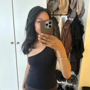 Svart one shoulder topp Josefine HJ x NAKD - Svart, tight one shoulder topp från Josefine HJ x NA-KD. Snygg minimalistisk design med asymmetrisk axel och figurnära passform. Perfekt för träning eller utgång❤️