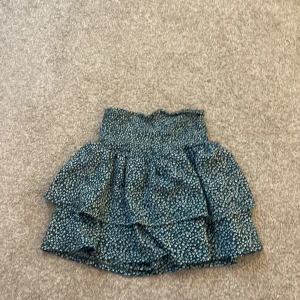 Blommig volangkjol från Zara  - Supersöt kort kjol från Zara med inbyggda shorts,blommigt mönster i mörkgrönt och vitt. Kjolen har bred resår i midjan och flera lager volanger som ger en riktigt snygg och livlig look. Perfekt för dig som gillar att sticka ut med detaljer och mönster.