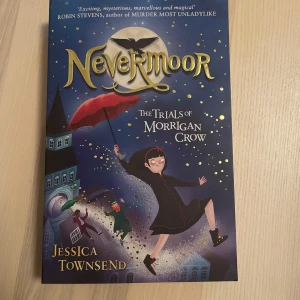 Nevermoor: The Trials of Morrigan Crow - En fantasifull bok på engelska av Jessica Townsend som handlar om Morrigan Crow som förs till den hemliga staden Nevermoor. Omslaget är blått med illustrationer av en flicka med röd paraply och magiska detaljer. Perfekt för dig som gillar äventyr och magi.