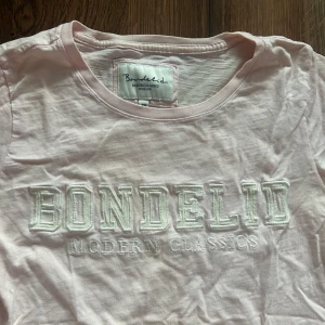 Ljusrosa t-shirt från Bondelid - Ljusrosa t-shirt från Bondelid med broderad logga och texten 'MODERN CLASSICS' framtill. Klassisk rund halsringning och korta ärmar. Perfekt för en gullig stil! 💓