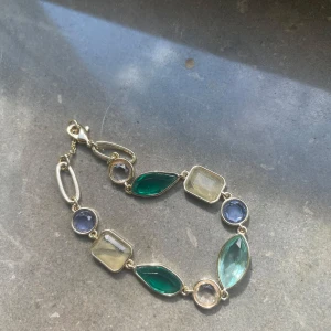 Armband med färgade stenar &Other stories - Snyggt armband med flera olika former av stenar i grönt, blått och transparent, infattade i guldfärgad metall. Stenarna är både runda, rektangulära och marquiseformade. Perfekt accessoar för att lyfta din outfit.