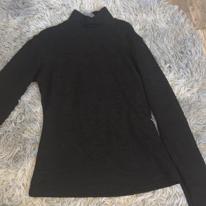 Svart polotröja från Amisu - Säljer en svart polotröja från Amisu med diskret struktur i tyget. Tröjan har lång ärm och en klassisk polokrage, perfekt för lager-på-lager eller som den är.