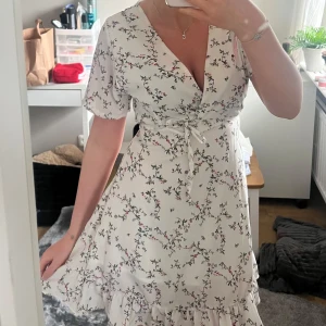 Vit blommig omlottklänning från Vera - Superfin vit omlottklänning från Vera med blommigt mönster i rosa och svart. Klänningen har korta ärmar, volangdetaljer nertill och knytband i midjan. Perfekt för sommarens alla tillfällen! Kommer ej ihåg storlek och ser inte heller på den, men skulle säga den passar som en S. Hör av er vid fler frågor och bilder!💛