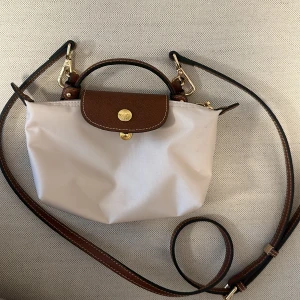 Longchamp väska mini - Säljer denna populära väskan från longchamp 💗har även köpt till ett långt band så att man kan ha den crossbody 💗 använd en gång! Perfekt skick! Endaste defekten är att två hörn är pyttelite mörkare