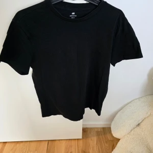 Svart t-shirt från H&M - En klassisk svart t-shirt från H&M med normal passform. T-shirten är kortärmad och passar perfekt till alla tillfällen. Enkel och stilren design som funkar till det mesta.